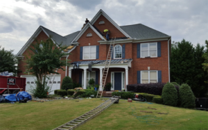 2 garage 2 story home with a ladder leaning against it and workers on the roof