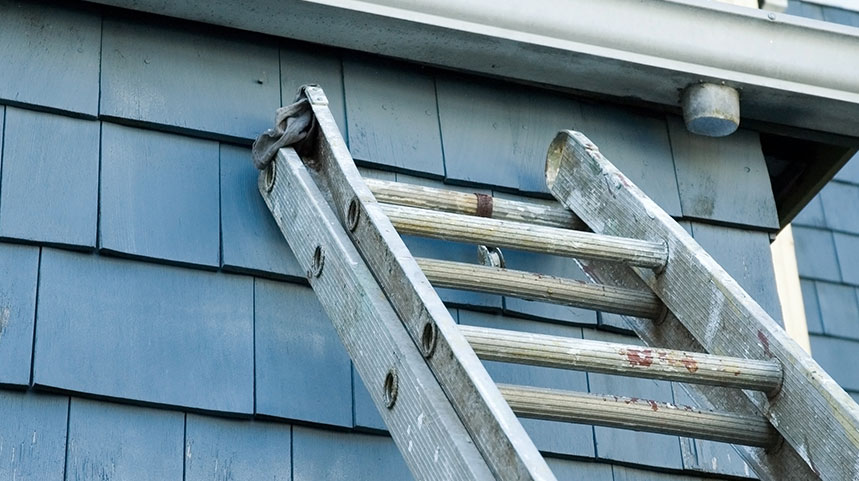 A ladder leaning up against a blue shingled house towards a gutter