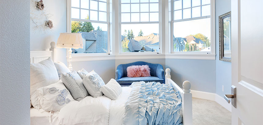 A bedroom with light, misty blue walls. and large windows.